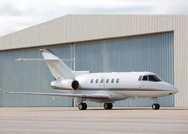 Private jet parked in front of steel aviation hangar