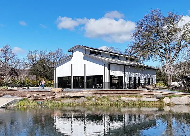 White barndominium reflected in a pond surrounded by trees